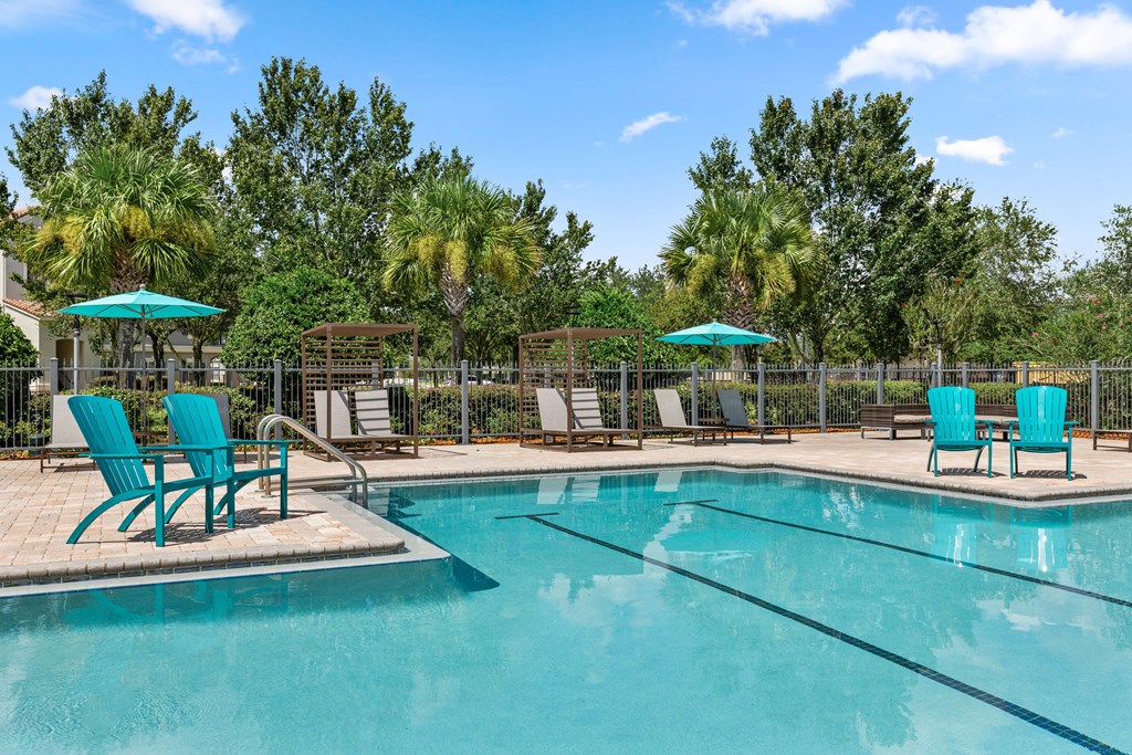 A pool surrounded by trees and chairs.