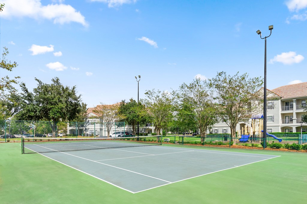A tennis court surrounded by trees and a building in the background.