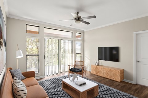 A living room with a brown couch, a coffee table, a television, and a ceiling fan.