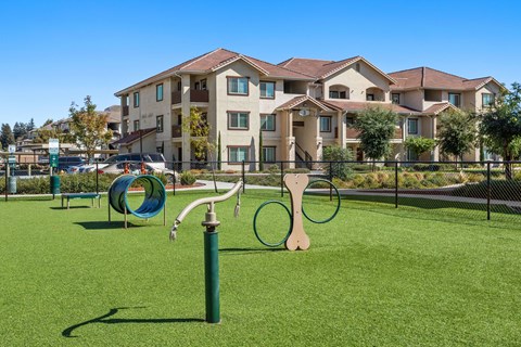 A playground with a green slide and a wooden swing set in front of apartment buildings.