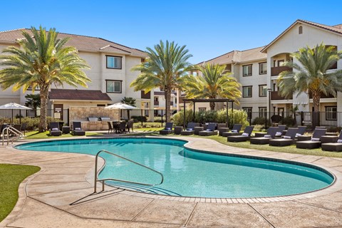 A swimming pool surrounded by palm trees and lounge chairs in front of a building.