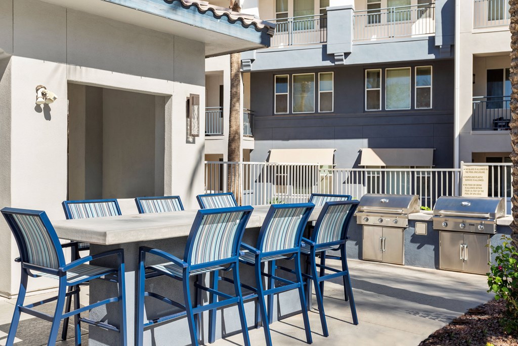 A table with blue chairs is in front of a building.