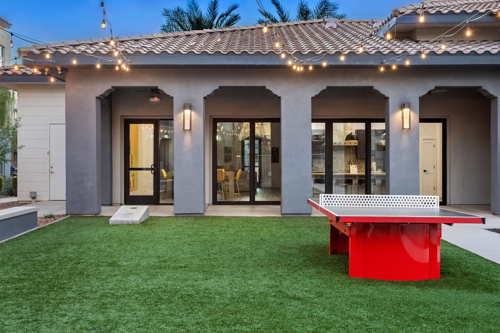 A red table is in front of a house with a white door.