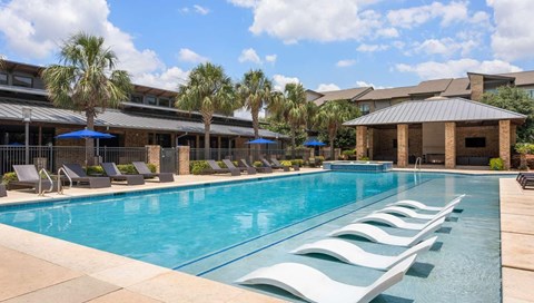 A large swimming pool with lounge chairs and umbrellas in front of a building.