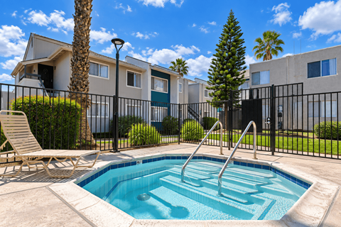 A pool surrounded by a black fence with a chair and a tree.