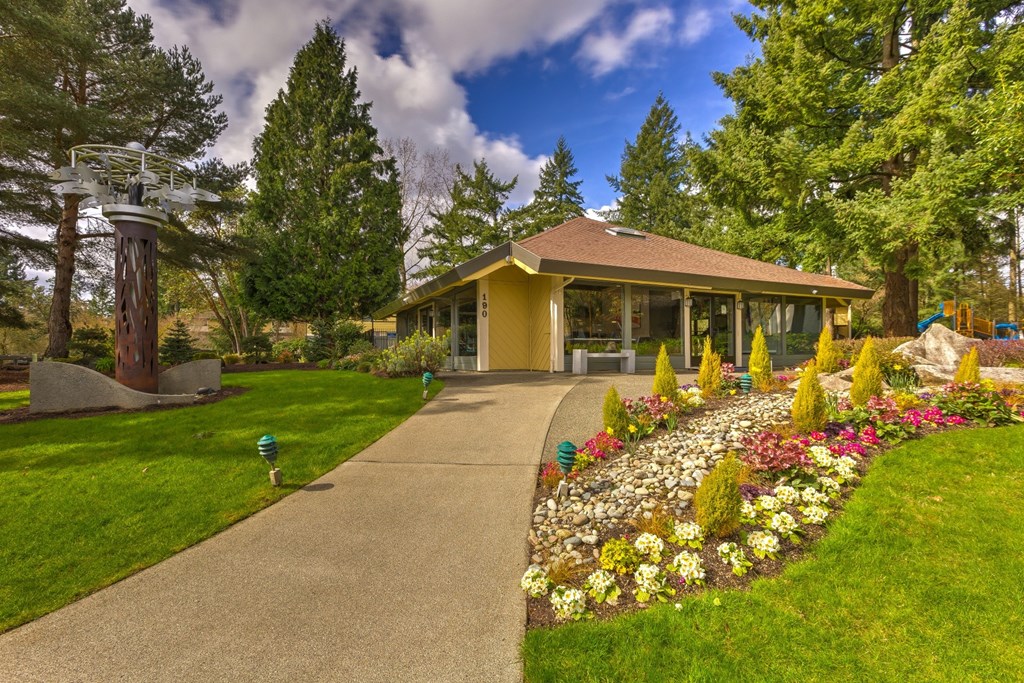 A yellow building with a brown roof is surrounded by a garden with a variety of flowers.