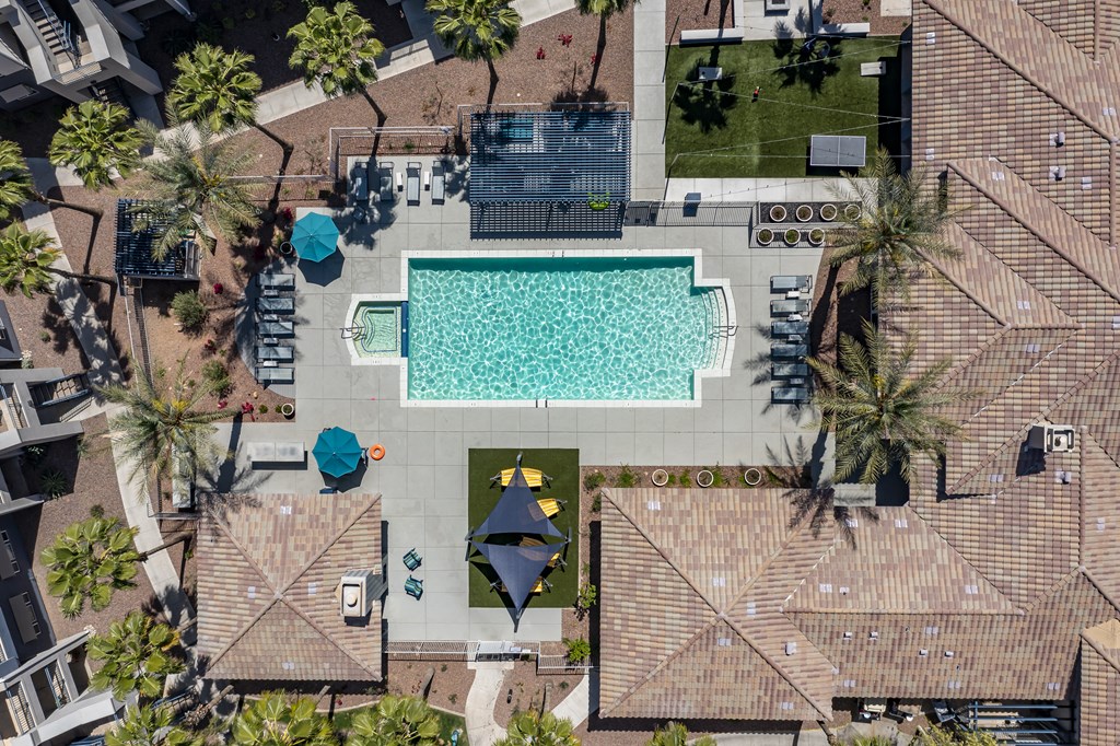 An aerial view of a swimming pool surrounded by palm trees and a few umbrellas.