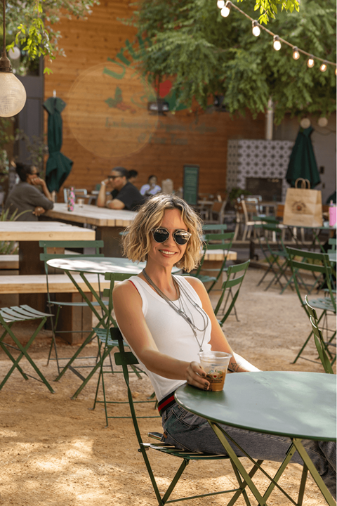 A woman in a white tank top is sitting at a table with a cup of coffee.