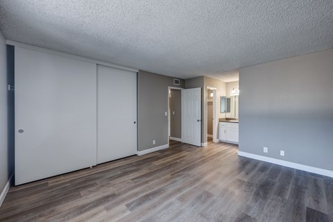 A room with a white ceiling and wooden flooring with a white door and a white cabinet.