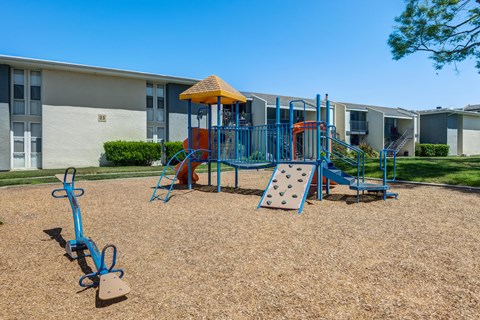 A playground with a blue swing set and a yellow umbrella.