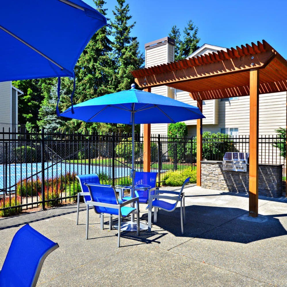 A blue umbrella is on a patio with a pool in the background.