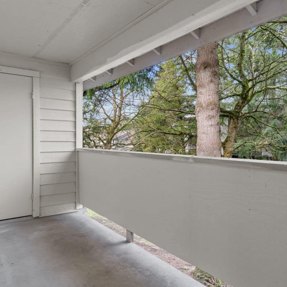 A white wooden deck with a white door and a view of trees.