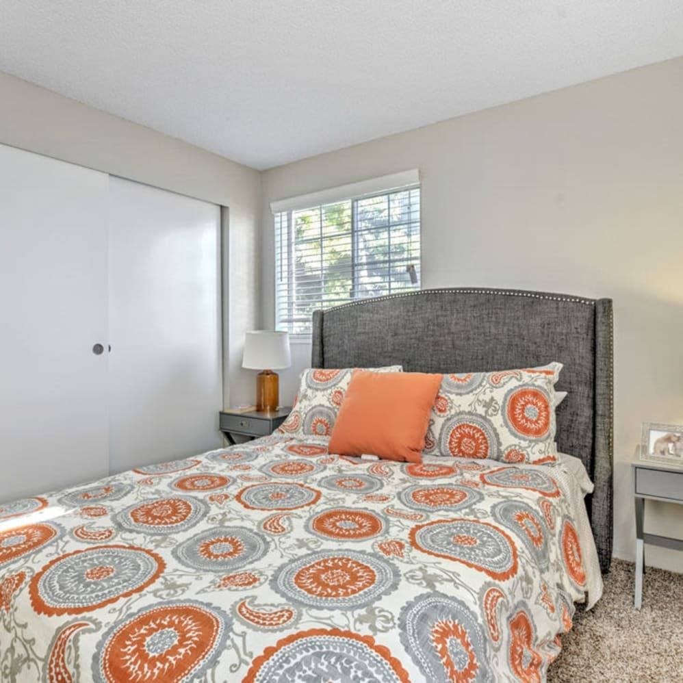 A bed with a grey headboard and orange and blue bedspread with matching pillows.