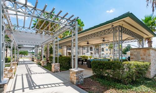 A walkway with a metal pergola and a stone wall.