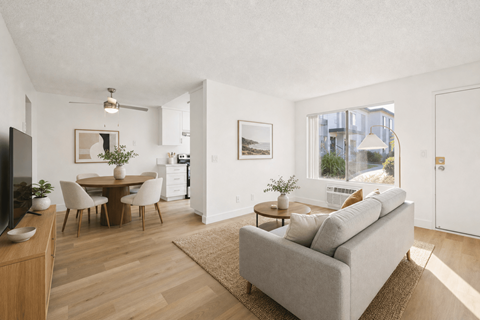 A living room with a grey couch, a wooden dining table with chairs, a television, and a rug.