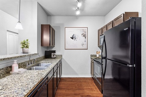 A black refrigerator is on the right side of a kitchen.