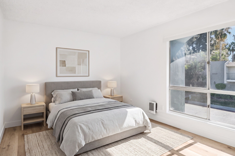 A bedroom with a large bed and a window overlooking a tree-lined street.