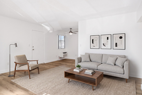A living room with a grey couch, a wooden chair, a coffee table, and three framed pictures on the wall.