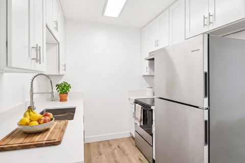 A kitchen with a refrigerator, oven, and a bowl of fruit on the counter.