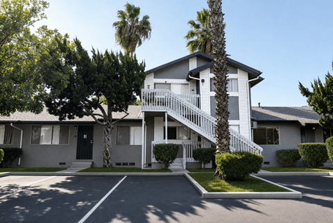 A white two-story house with a balcony and a palm tree in front.
