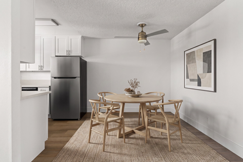 A dining room with a table set for two and a refrigerator in the corner.