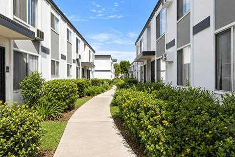 A long concrete walkway separates a row of white buildings.