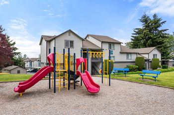 A playground with a red slide and yellow and blue play structures in front of a building.