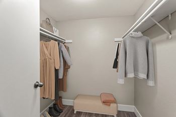 A small closet with a bench and clothes hanging.