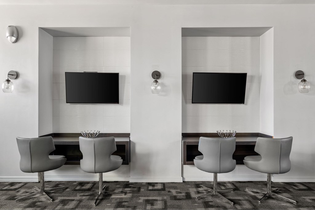 Two chairs are placed in front of two TVs on a wall.