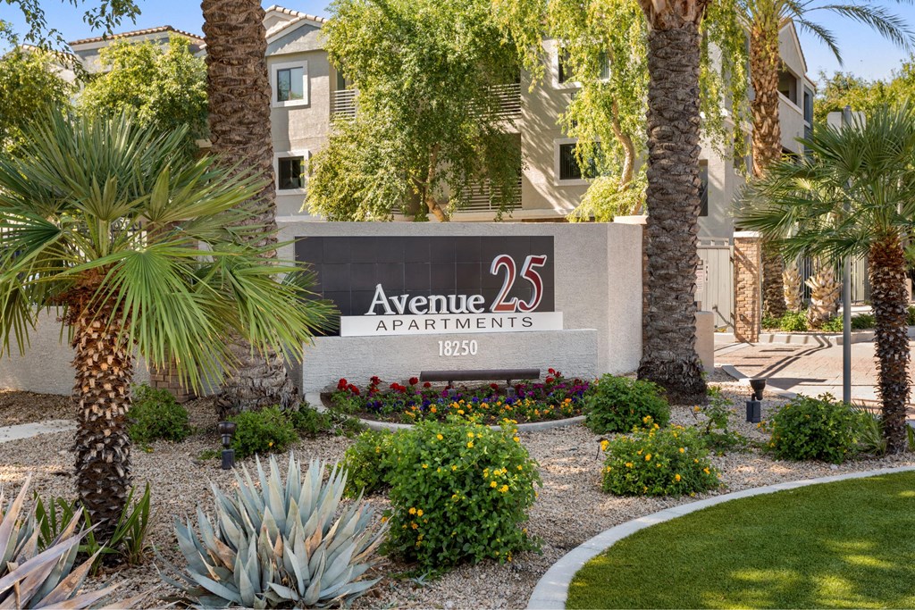 A sign for Avenue 25 Apartments is surrounded by plants and trees.