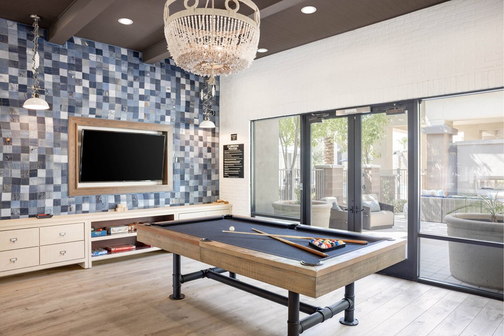 A pool table is in the middle of a room with a tv and a chandelier.