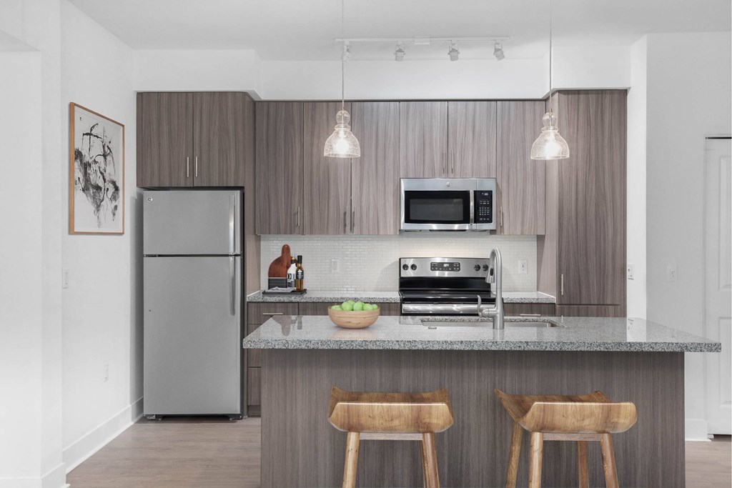A modern kitchen with a refrigerator, microwave, oven, and a counter with two chairs.