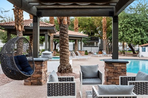 A patio with a hanging chair and a pool in the background.