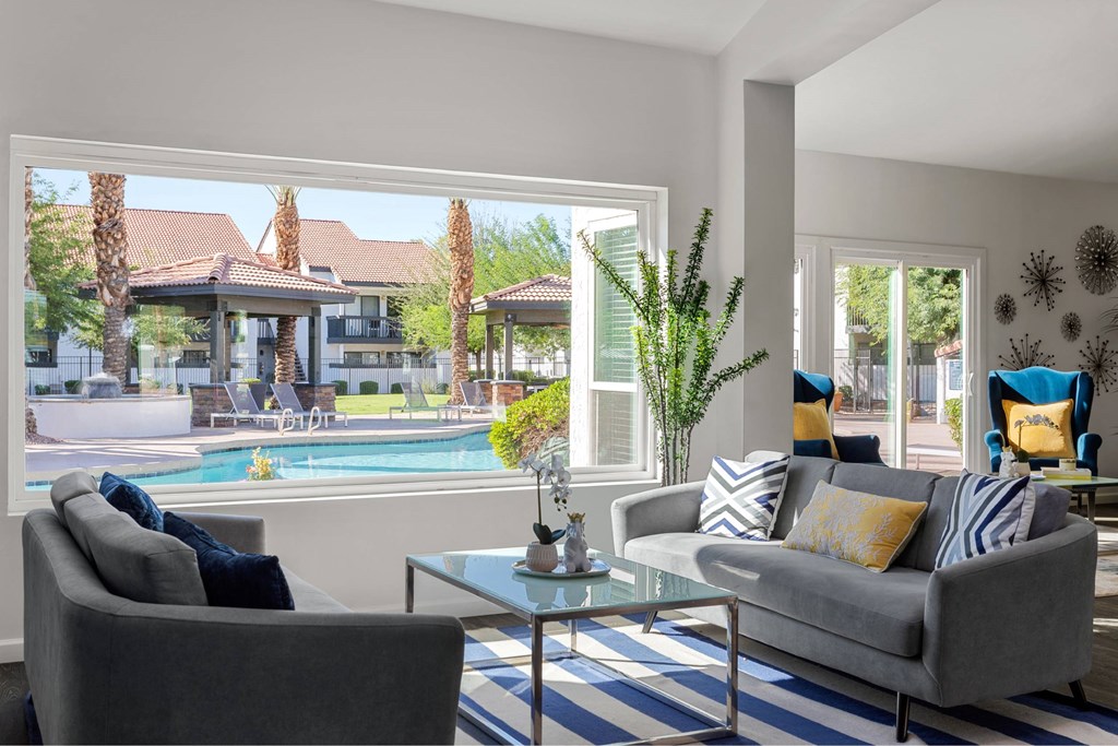 A living room with a grey couch, a glass table, and a view of a pool and a building outside.