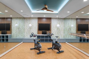 Two stationary bikes are in a room with a patterned wallpaper and a ceiling fan.