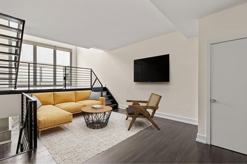 A living room with a yellow sofa and a black metal staircase.
