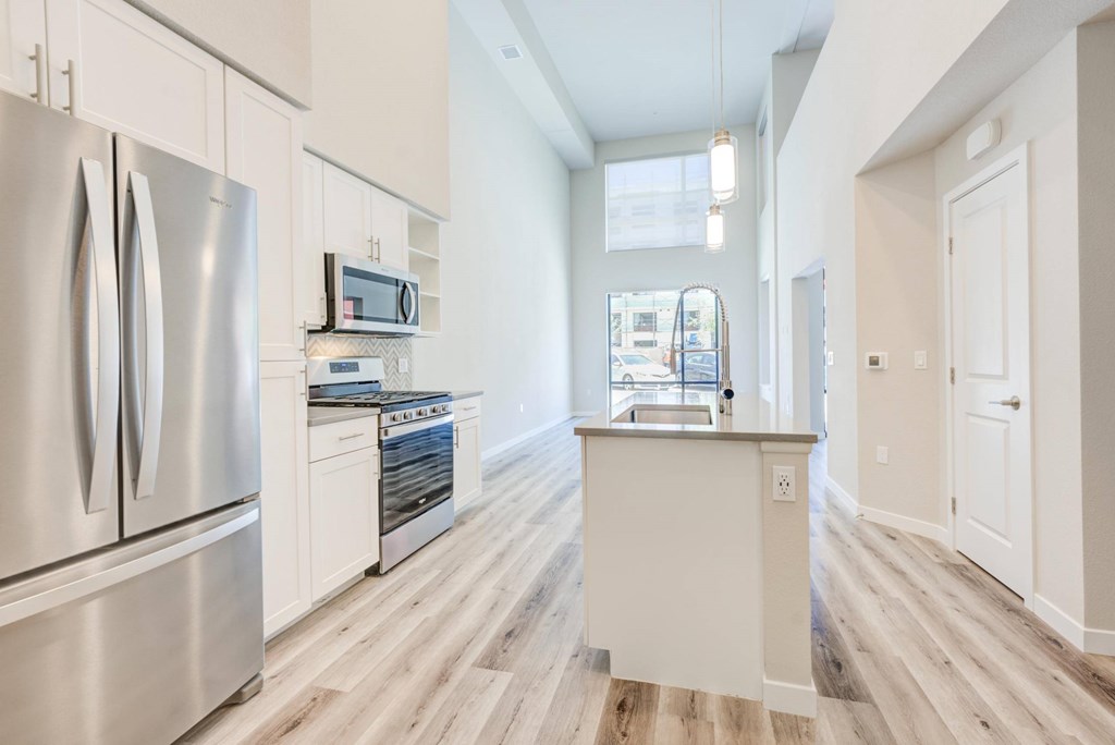 A modern kitchen with a stainless steel refrigerator and wooden flooring.