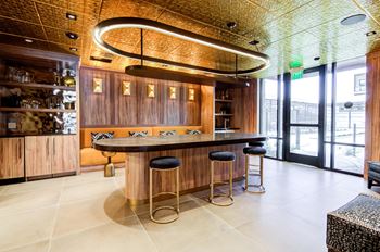 A bar with a wooden counter and stools is illuminated by a circular light fixture.