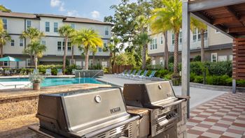 Two grills are in the foreground of a resort with a pool and palm trees.