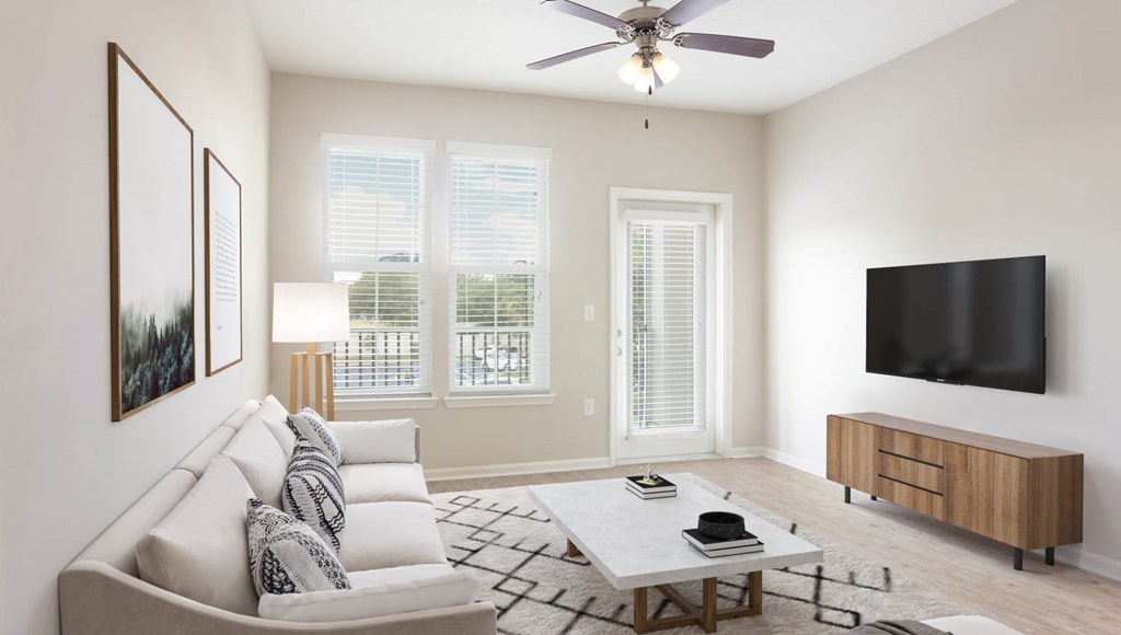 A living room with a grey couch, a coffee table, a flat screen TV, and a ceiling fan.