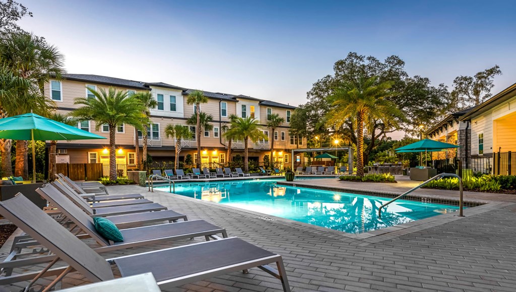 A pool surrounded by lounge chairs and umbrellas in front of a building.