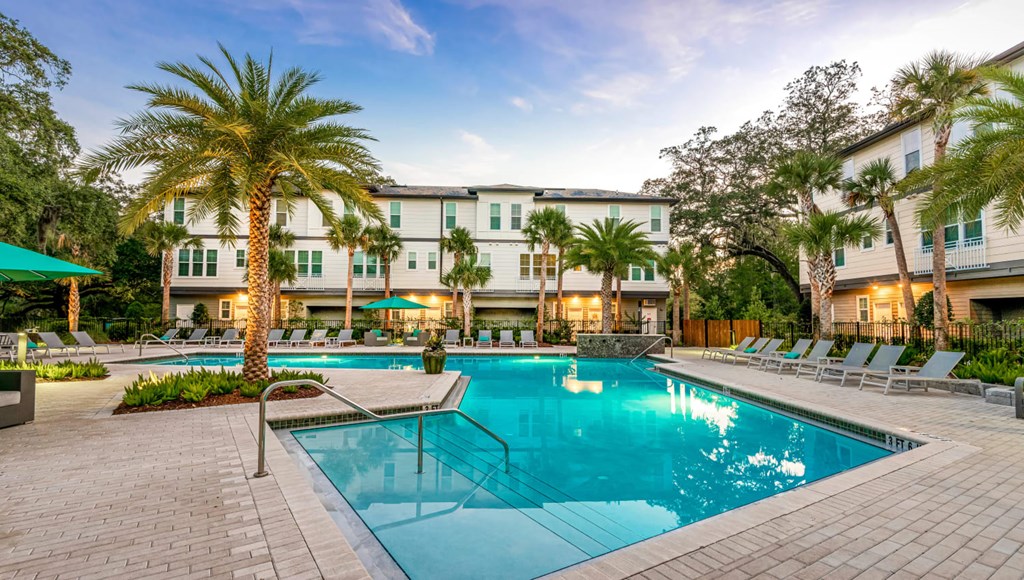 A swimming pool surrounded by lounge chairs and palm trees in front of a hotel.
