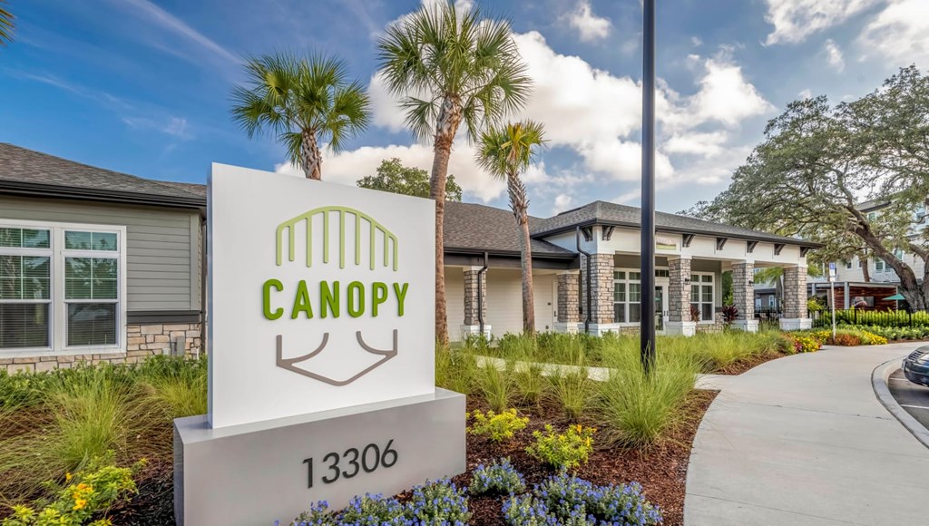 A sign for Canopy with a house in the background.