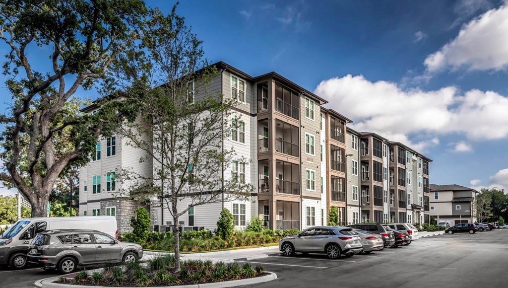 A row of apartment buildings with cars parked in front.