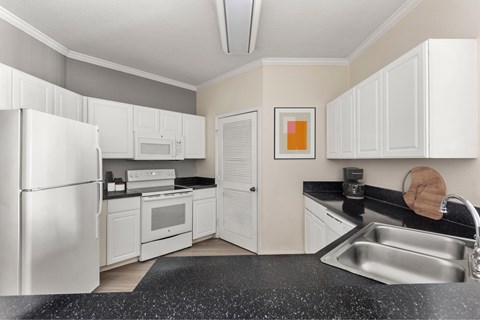 A kitchen with white cabinets and a black countertop.