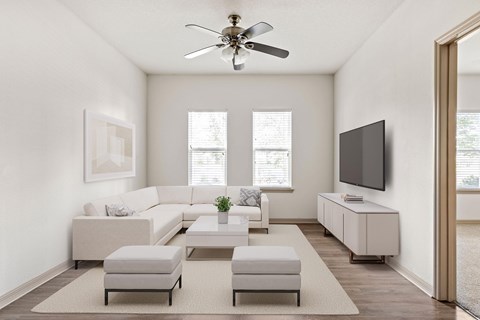A living room with a white sofa set, a television, and a ceiling fan.