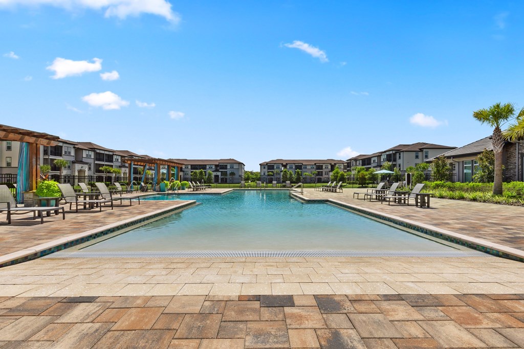 A large swimming pool surrounded by a brick patio and lounge chairs.