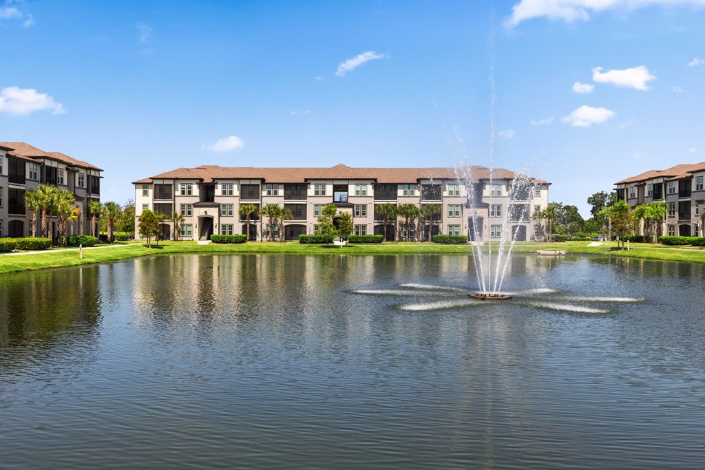 A fountain in the middle of a lake in front of a building.