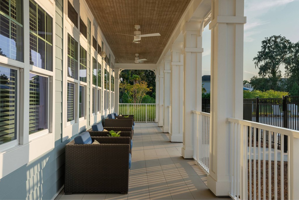 A long white porch with brown chairs and a ceiling fan.