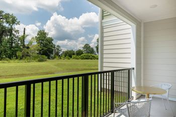 A balcony with a table and chairs overlooking a green field.